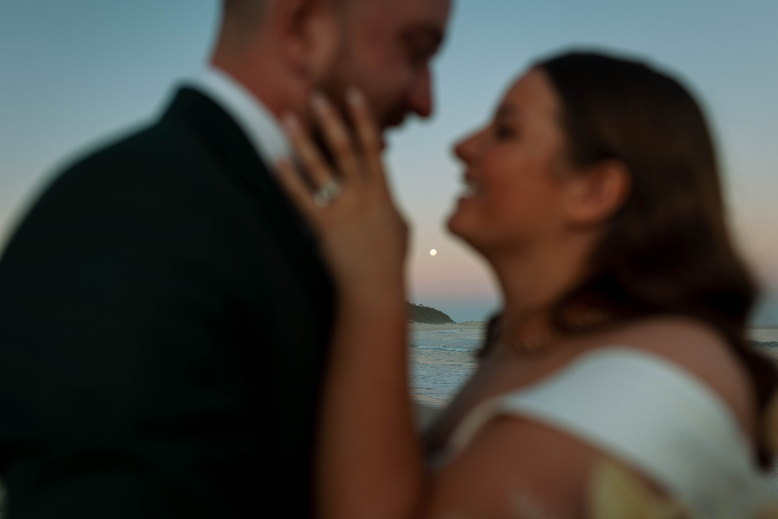 husband and wife kissing at moonrise on the beach at sunset in Fingal Bay