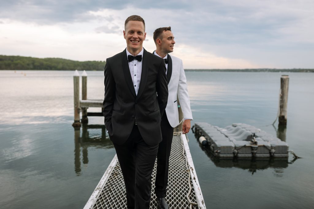 husband and husband holding hands walking on a jetty at raffertys resort during the groom photo shoot
