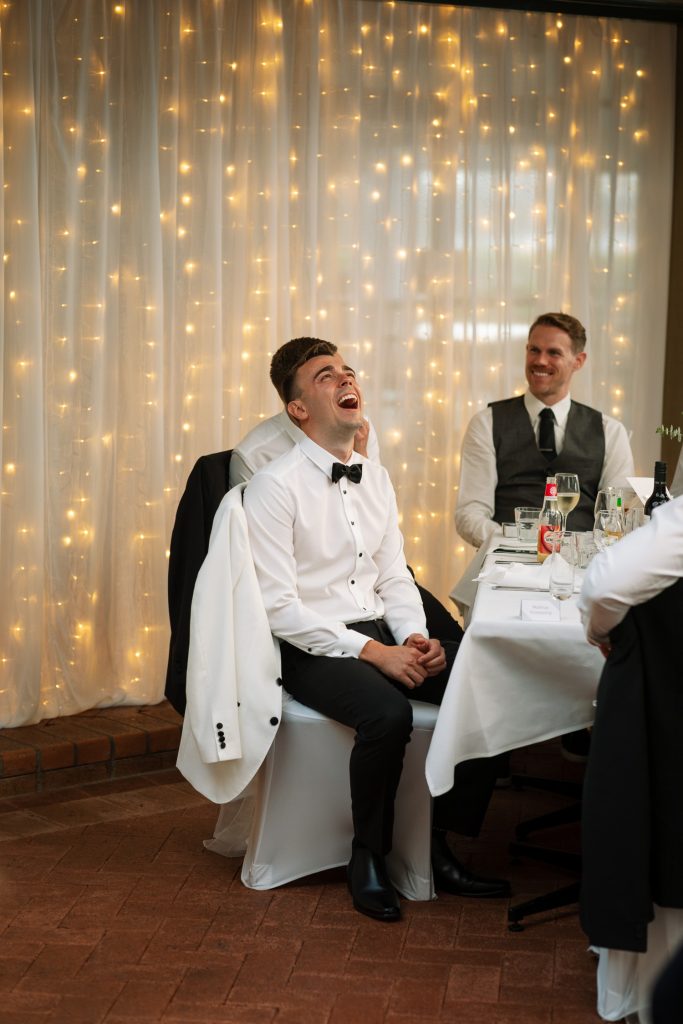 husband and husband laughing at speeches at raffertys resort during the wedding reception