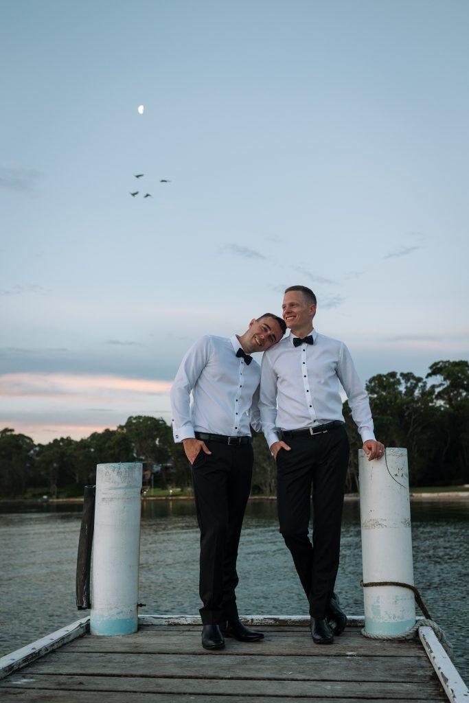 husband and husband getting sunset photos on the jetty at their wedding at raffertys resort