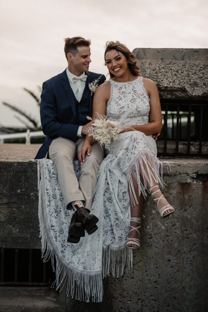 bride and groom sitting on the wall Newcastle beach