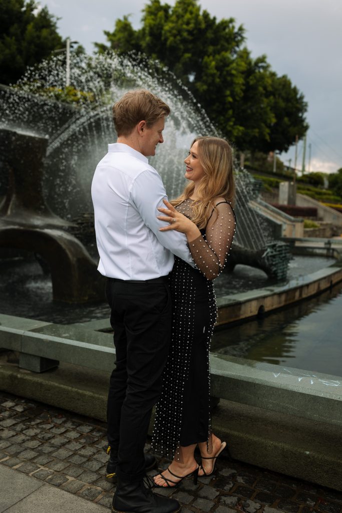 couple hugging in front of water fountain in Newcastle on their engagement session