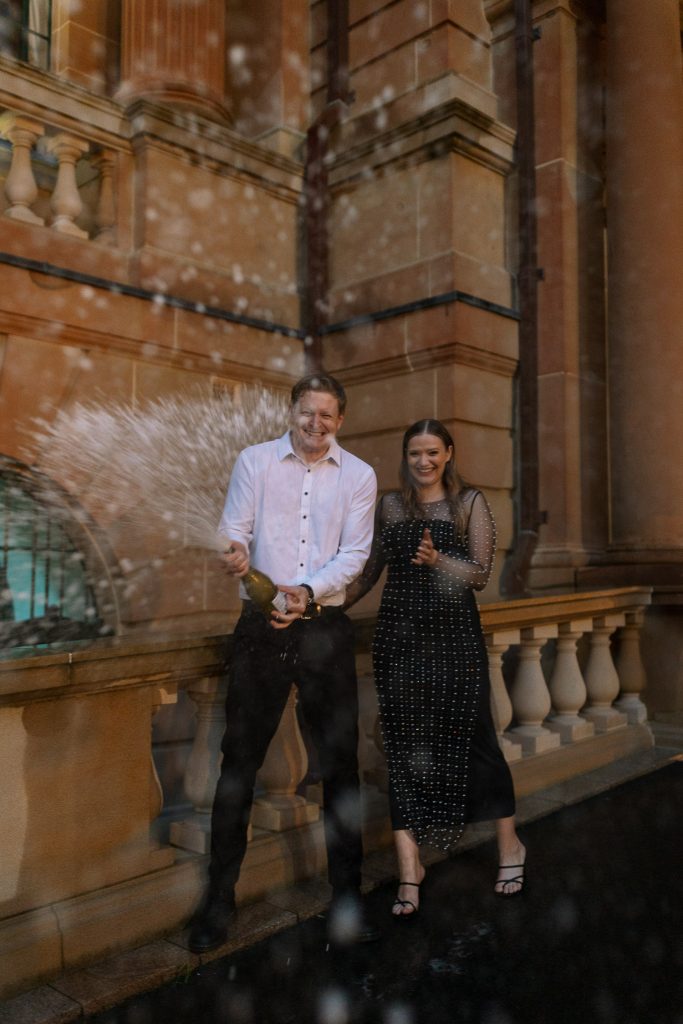 couple outside on the steps at custom house spraying champaign in Newcastle on their engagement session