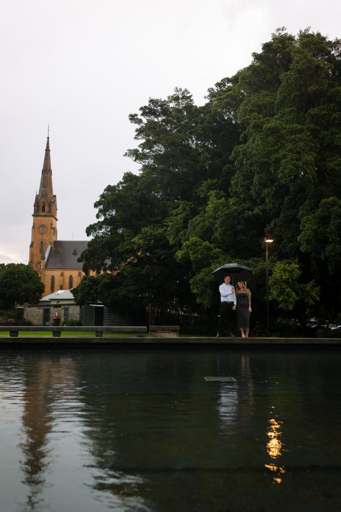 couple holding hands in the rain with an umbrella in Newcastle on their engagement session