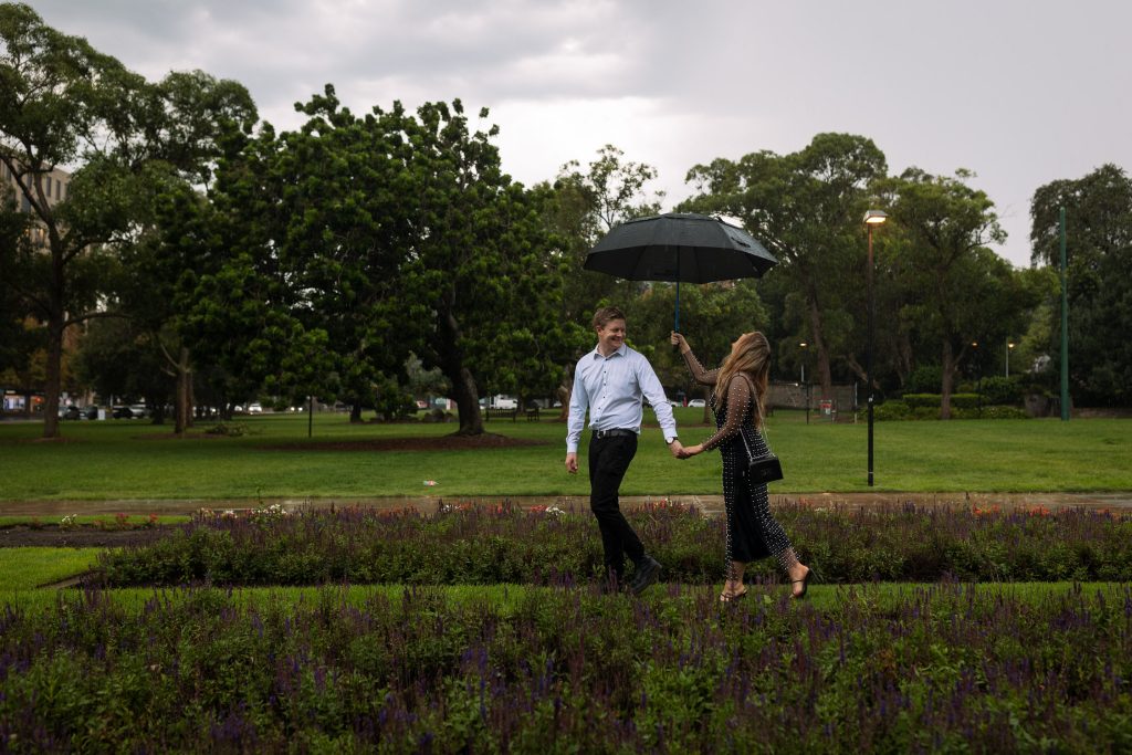 couple walking holding hands in the rain with an umbrella in Newcastle on their engagement session
