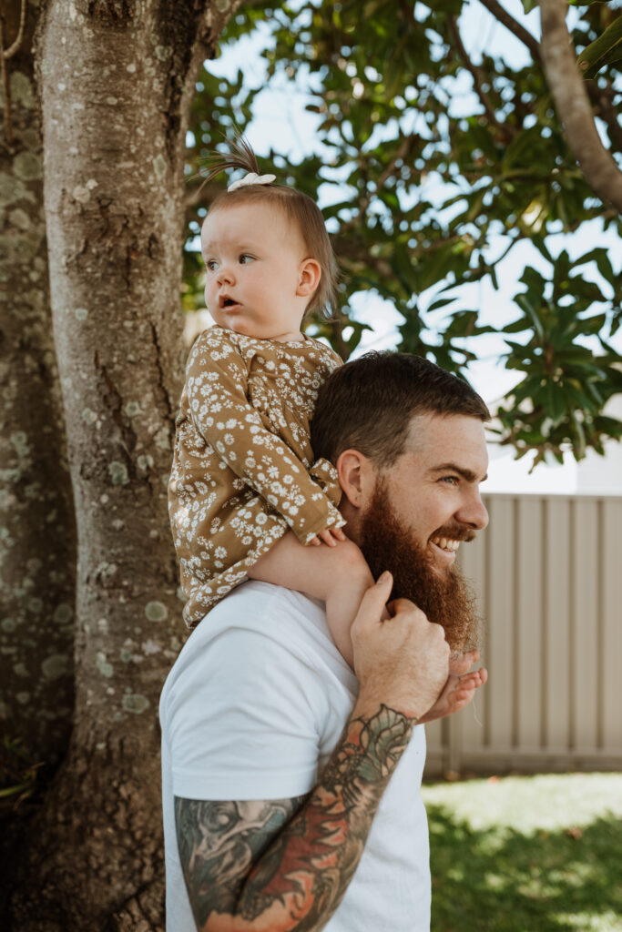 baby on dads shoulders in the garden by a tree