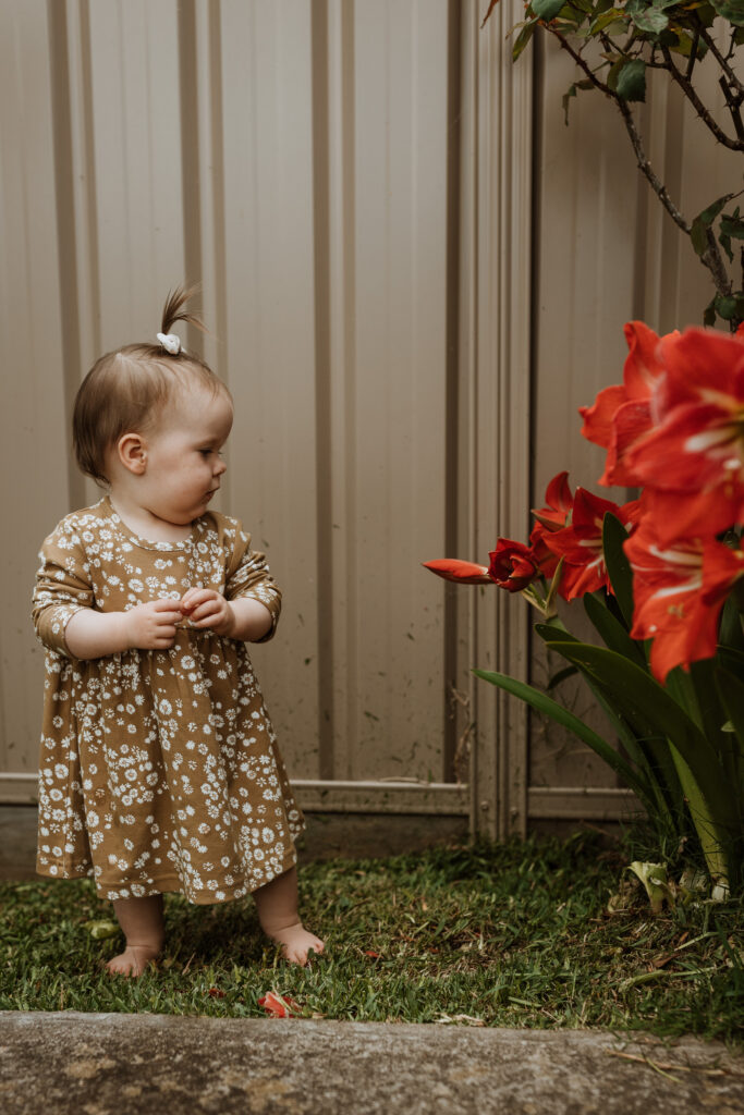 baby in the garden next to colourful flowers looking at them