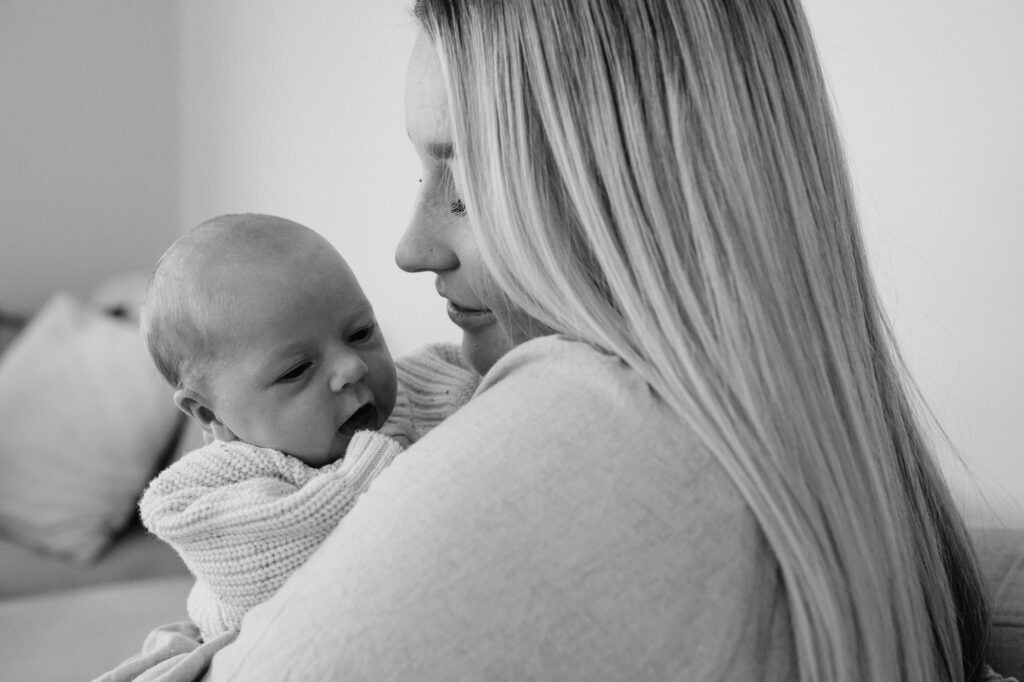 Mum cuddling baby in arms kissing her forehead in black and white