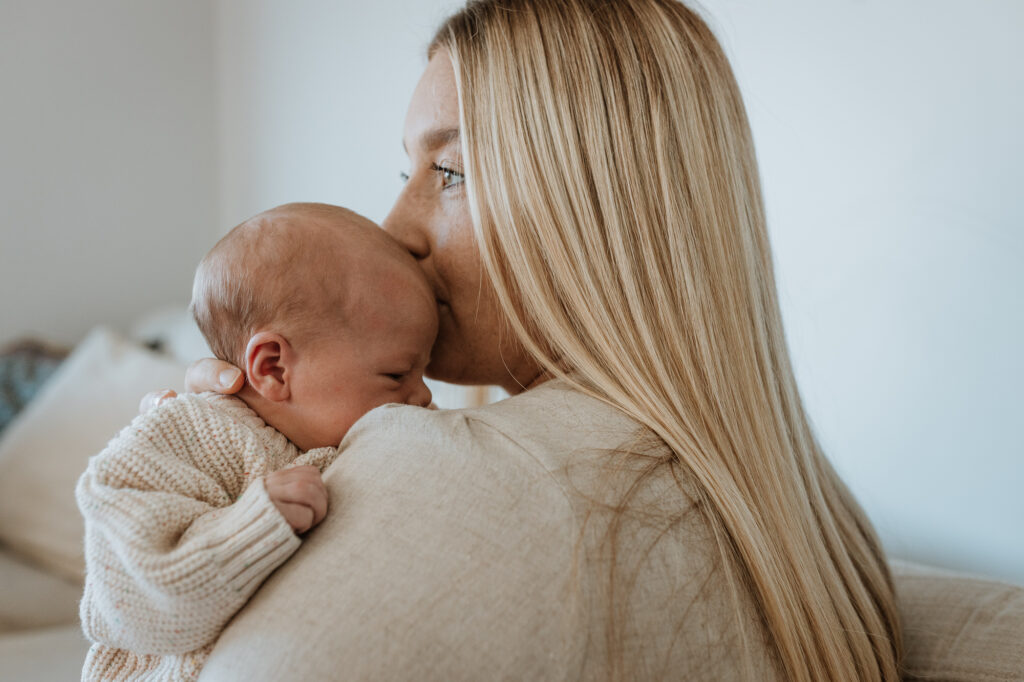 Mum cuddling baby in arms kissing her forehead