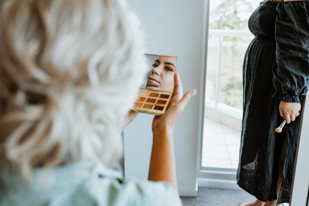Bride getting ready and having her make up applied and looking in the mirror