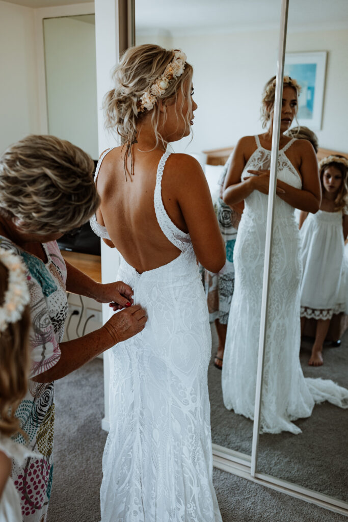 bride getting her dress on in the mirror with help from her mother