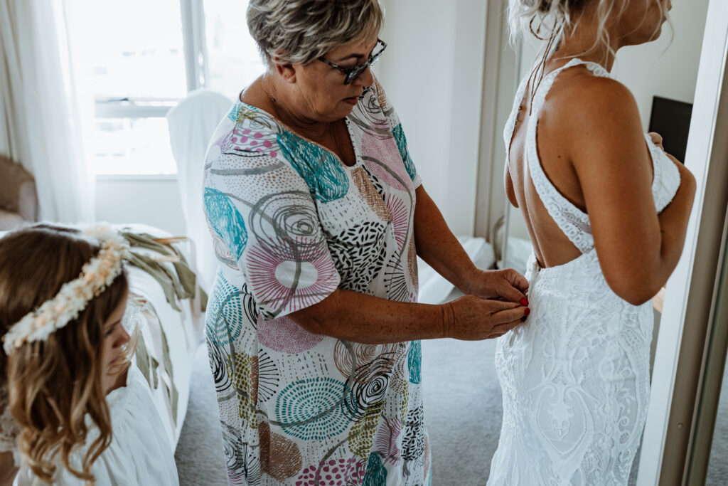 bride getting her dress on in the mirror with help from her mother