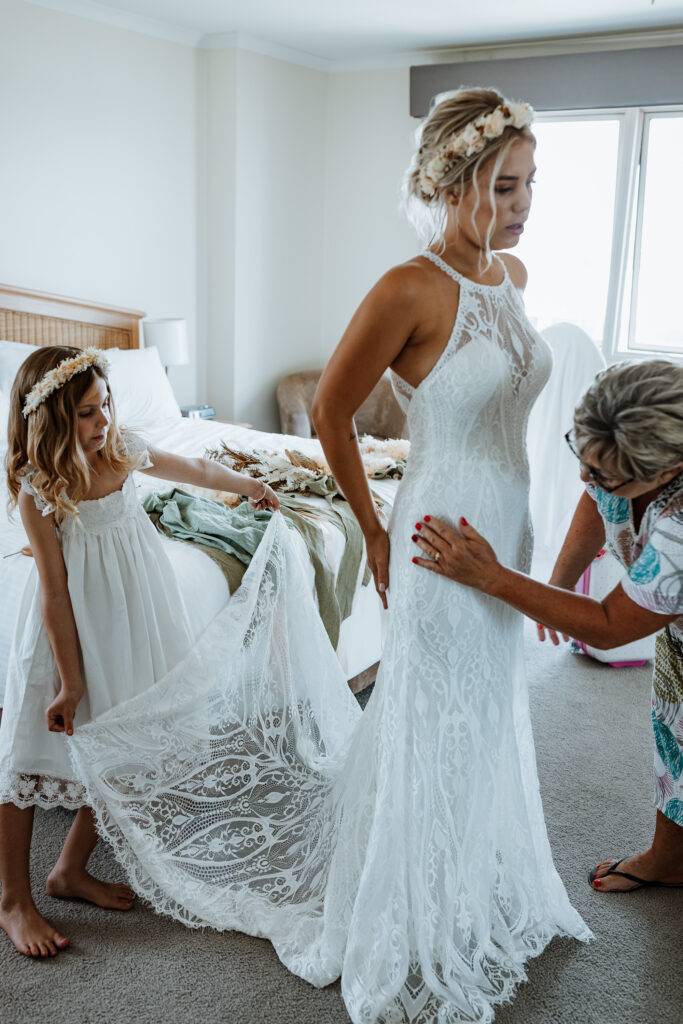 bride getting her dress on in the mirror with help from her mother