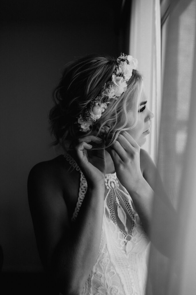 bride putting her earrings in before the wedding in black and white