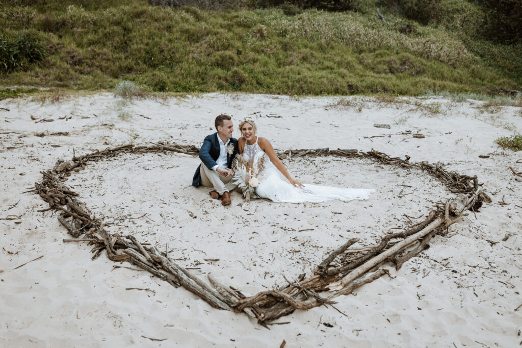 husband and wife photo shoot on the beach in Port Macquarie sat on the sand in a heart