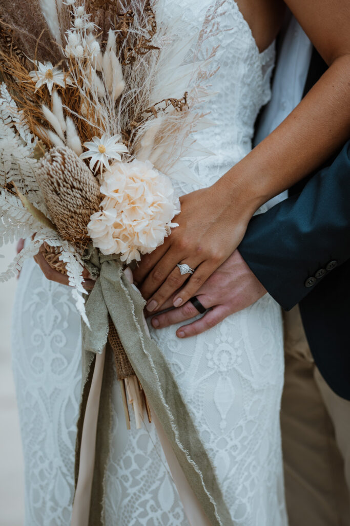 husband and wife photo shoot on the beach in Port Macquarie with the bridal party and their wedding rings and their dried wedding flowers