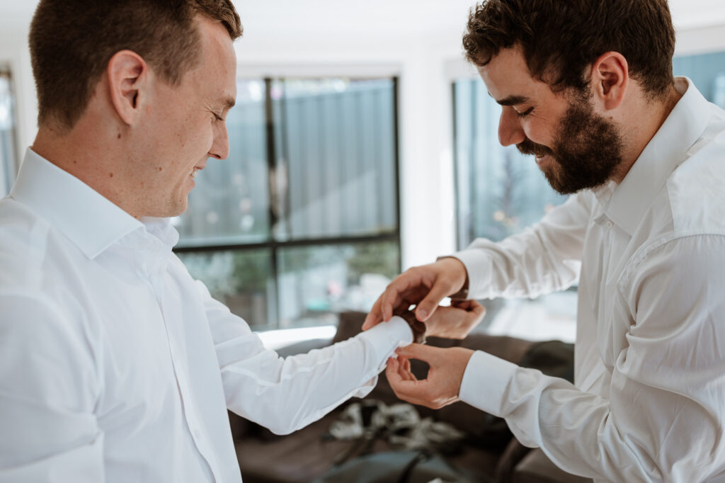 groomsmen getting ready at the grooms house. Putting shirts on and fastening up the cufflinks