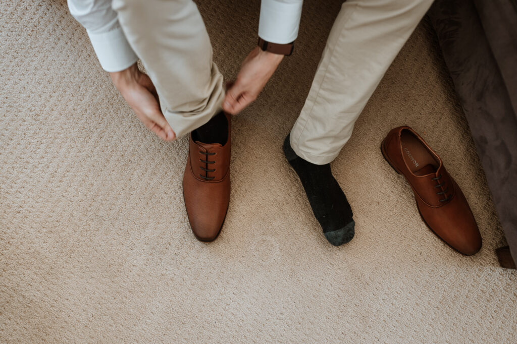 groom putting shoes on at the house whilst getting ready