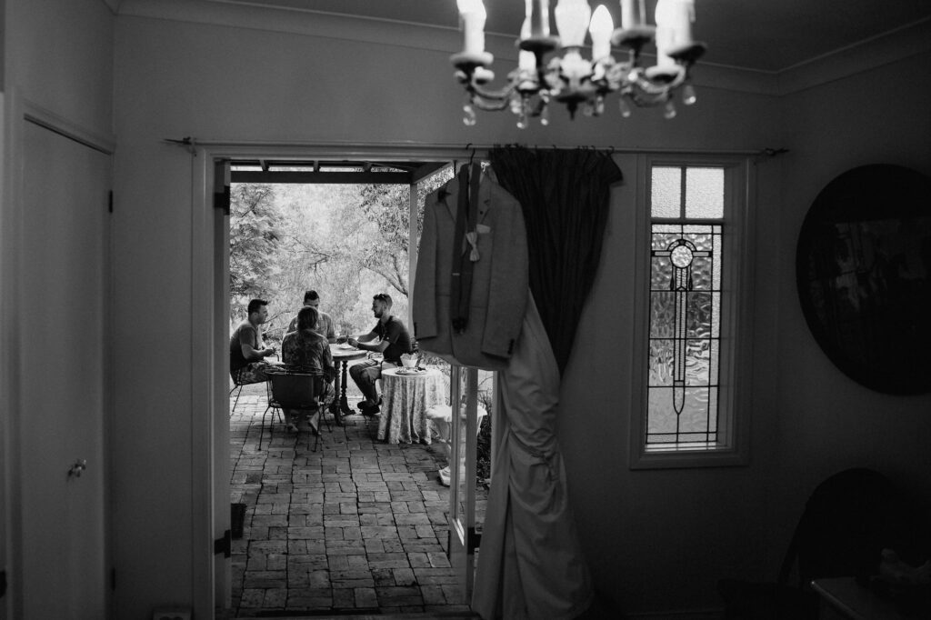 groom's suit hanging up over the door way with groomsmen in the shot