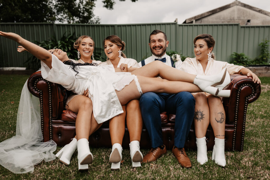 bride laying down across the bridal party on the couch in the garden