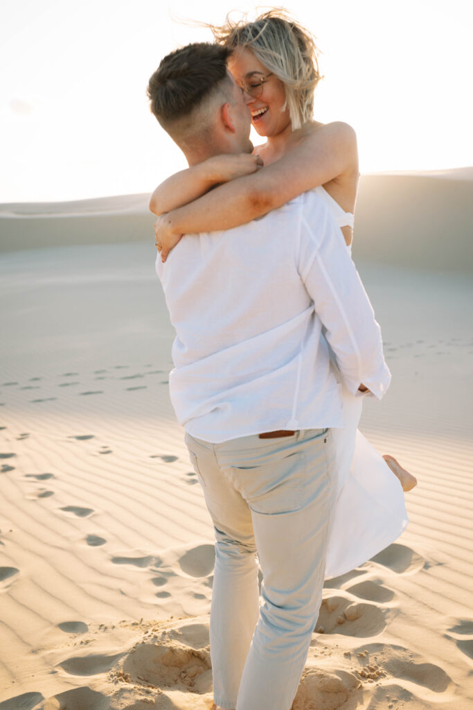 Engagement session sunset at Stockton sand dunes being picked up and span around