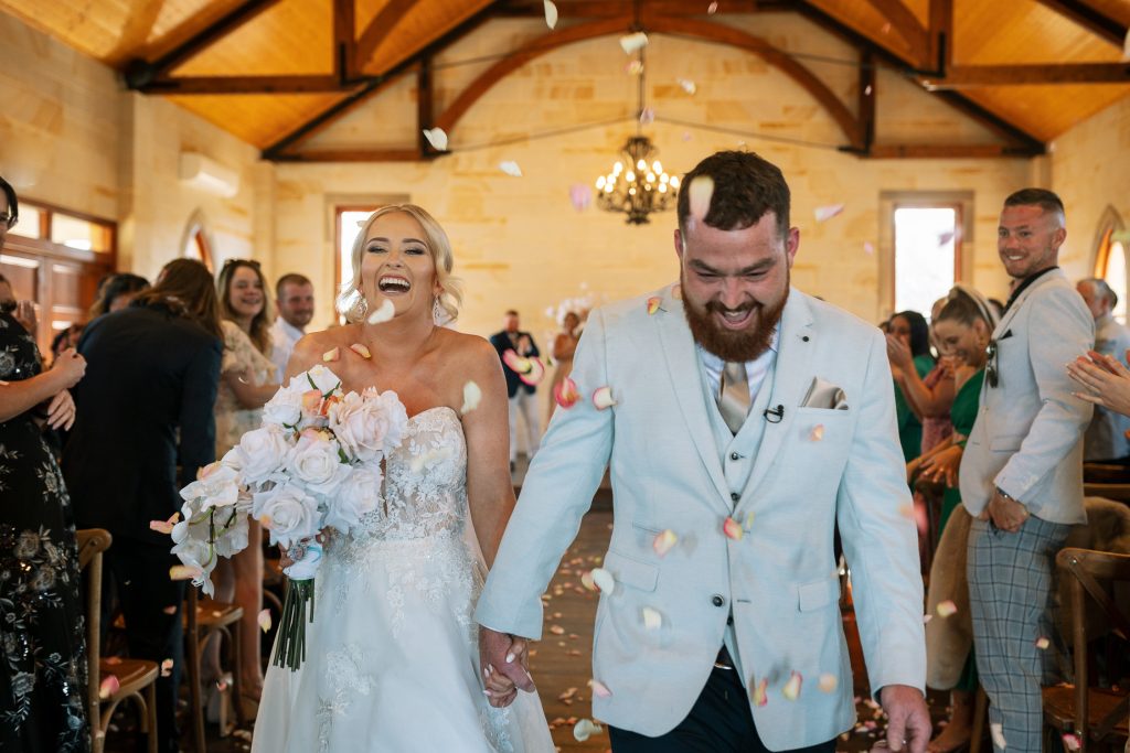 husband and wife getting married walking out under confetti in a chapel in the hunter valley