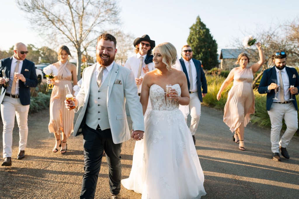 husband and wife walking with their bridal party behind them drinking and cheering