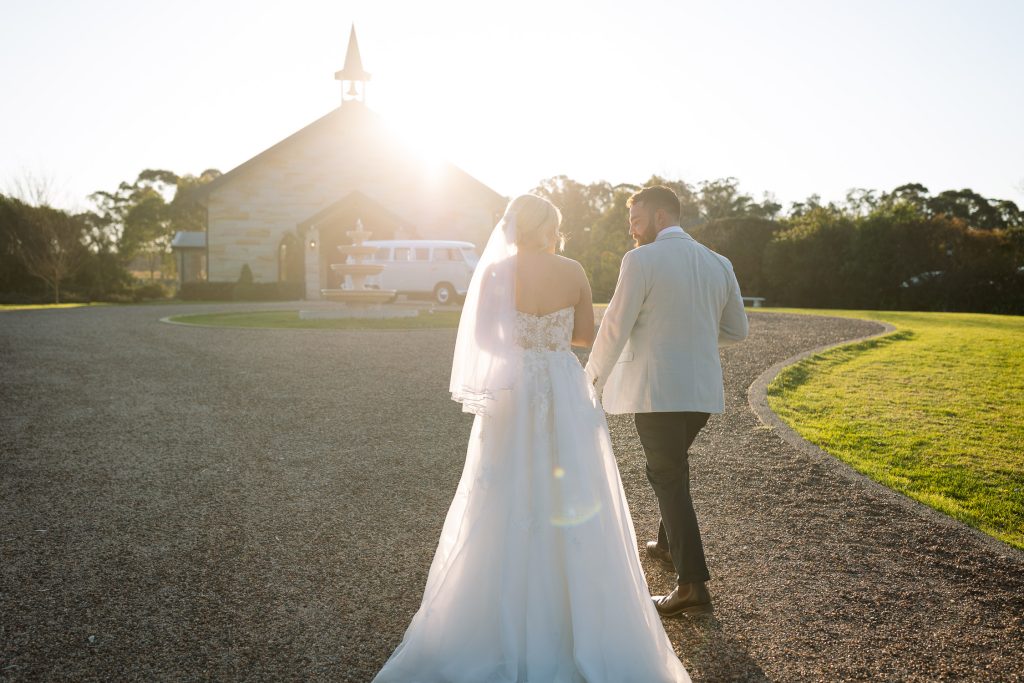 husband and wife walking towards the Chapel with the sunset behind them in the hunter valley