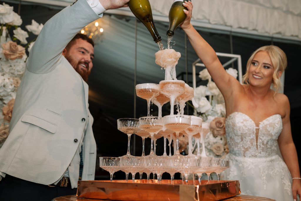husband and wife pouring champaign in to a campaign tower at a wedding in the hunter valley