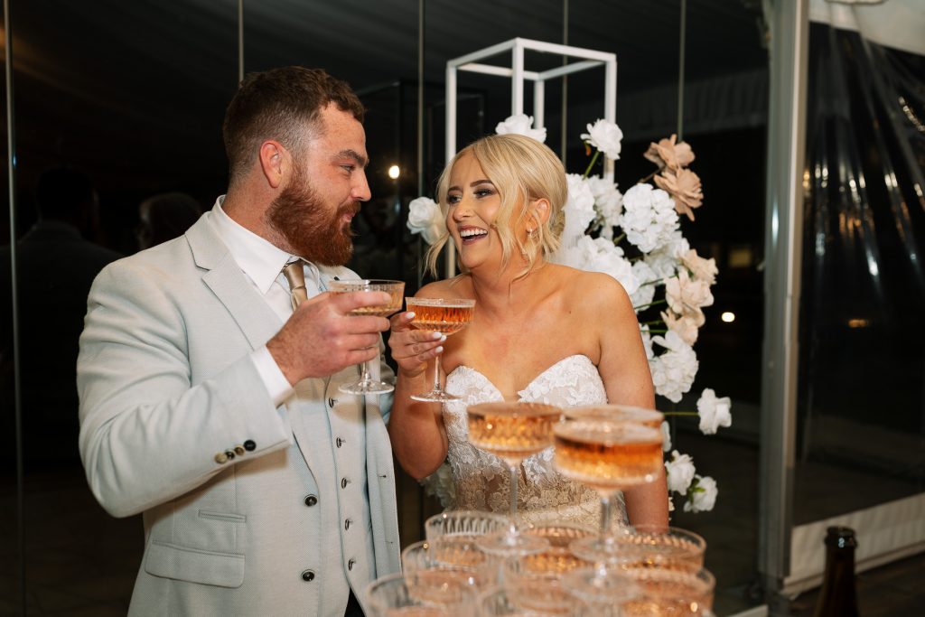 husband and wife pouring champaign in to a campaign tower at a wedding in the hunter valley